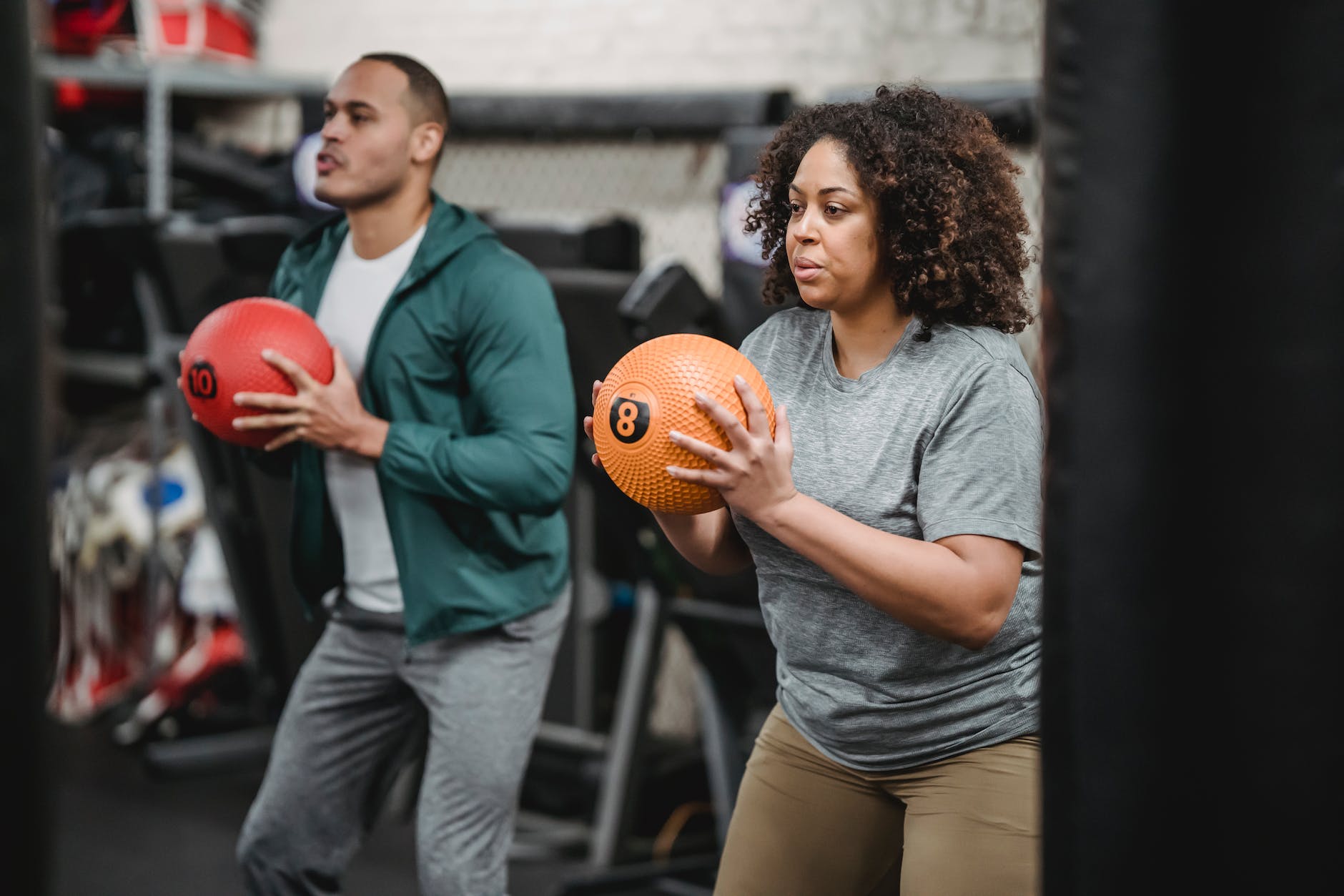 concentrated young diverse trainer and athlete exercising with medicine balls in gym